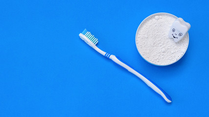 A cheerful tooth figure in a jar with tooth powder and a toothbrush on a blue background. The view from the top. Flat lay.