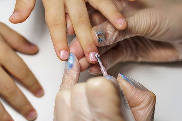Professional manicure for child. Cosmetologist applies healing and firming varnish on nails on child's fingers. Shooting close-up.