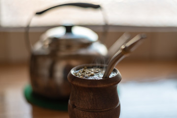 Filled smoking mate with a kettle on a watermelon trivet over a wooden counter and half window on the background