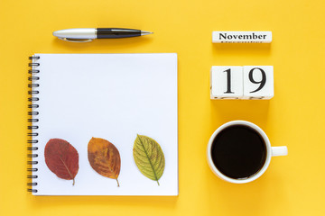 Autumn composition. Wooden calendar November 19 cup of coffee, empty open notepad with pen and yellow oak leaf on yellow background. Top view Flat lay Mockup Concept Hello November