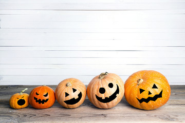 Halloween pumpkins with drawn faces on a wooden table on a background of white boards.