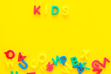 Early childhood development concept. Word kids written by plastic letters of toy alphabet on yellow background top view copy space
