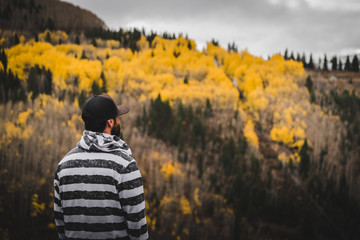 A man looking out into the distance of a mountain covered in fall foliage. 