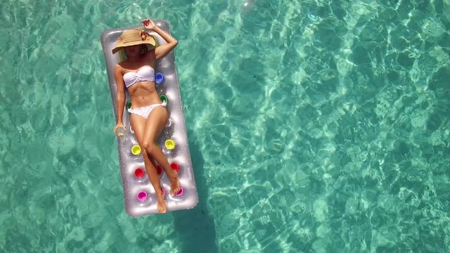 Aerial - Closeup of a young woman relaxing on inflatable mattress in crystal cle