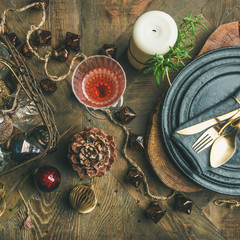 Christmas or New Year eve holiday table setting. Flat-lay of plates, silverware, champaigne in glass, pine cone, candle and toy festive decorations over vintage table background, top view, square crop