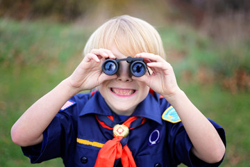 Young Tiger Cub Scout Smiling at Camera Through Binoculars - obrazy, fototapety, plakaty