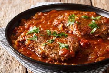 Juicy cube Swiss steak fried and slowly stewed in a spicy tomato sauce with vegetables close-up....