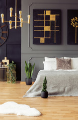 Gold and black painting hanging above bed with bright sheets in real photo of dark bedroom interior...