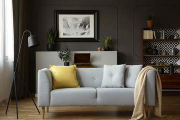 Comfy sofa with grey and yellow pillows, lamp, painting and cupboard in a living room interior....