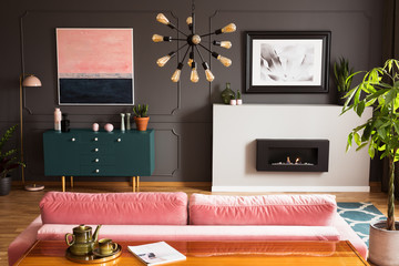 Poster above fireplace in grey living room interior with plant next to pink sofa and table. Real...