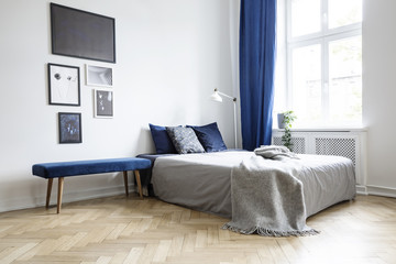 Natural light coming through a large window into a white and navy blue bedroom interior with cozy...