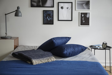 Minimalist bedroom interior with a warm wool blanket and navy blue pillows on a double bed by a...