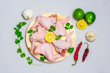 Wooden board with raw chicken wings with skin and ingredients lemon, cilantro, garlic, chili,pepper for cooking on gray concrete background Flat lay Top view Healthy food