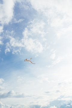 White kite flying against the blue sky full of clouds. Vertical image