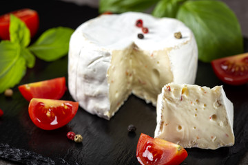 Camembert cheese with basil leaves and cherry tomatoes on a dark slate
