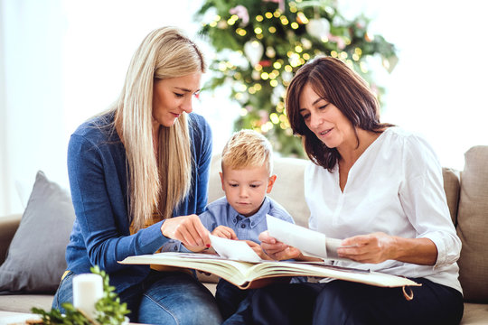 A small boy with mother and grandmother looking at photos at home at Christmas time.