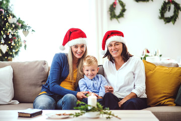 A small boy with mother and grandmother with Santa hat at home at Christmas time.