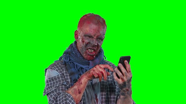 Halloween theme horrible scary zombie in clothes uses the phone isolated over green screen background