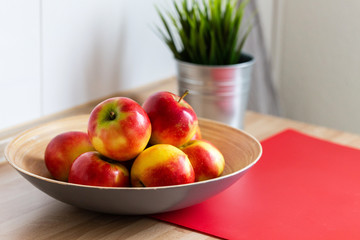 rot gelbe &auml;pfel in einer obstschale,mit einem roten schneidebrett und einer gr&uuml;nen pflanze im hintergrund