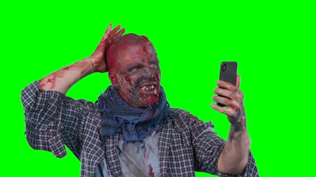 Man in zombie makeup makes selfie phone isolated over green screen background