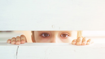 Frightened child is spying through a wooden fence. Scared child boy. Human emotion, facial...