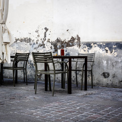 empty table and chairs in front of an old wall