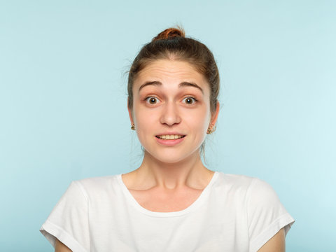 Shocked Surprised Caught Off Balance Astounded Girl. Facial Emotion. Young Beautiful Woman With A Hair Bun On Blue Background.