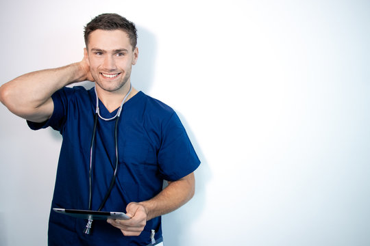 Good Looking Male Doctor Or Nurse In Blue Scrubs, Holding Digital Tablet And Laughing