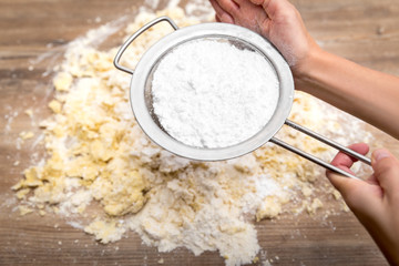 Frau beim durchsieben von Puderzucker auf einen Kuchenteig oder Plätzchenteig