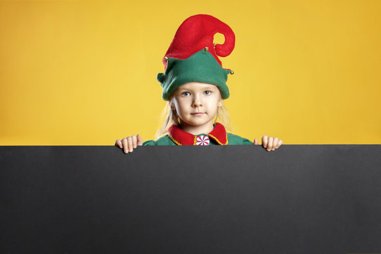 Christmas photo. Little girl in a Christmas elf costume and in a red cap. Place for text on a black background, copy space.
