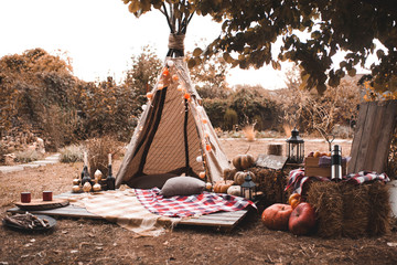 Stylish wigwam with lights, pumpkins and stack of hay outdoors. Autumn season. © morrowlight
