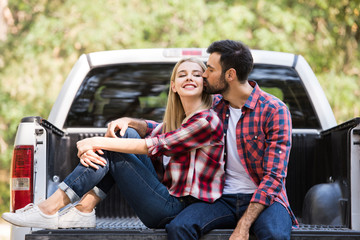 man kissing cheek of happy girlfriend while sitting on pickup truck © LIGHTFIELD STUDIOS