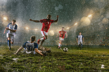 Soccer players performs an action play on a professional night rain stadium. Dirty players in rain...