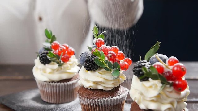 Baker decorating tasty cupcake. Icing sugar sprinkled on cake
