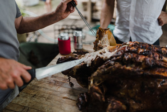 Man slicing hog roast on table, cropped