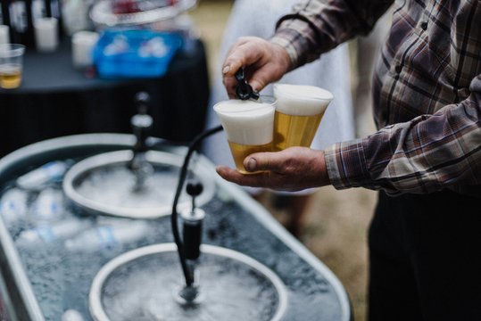 Man pouring beer from keg in cooling bath at barbecue, cropped