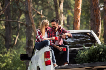 happy man pouring wine into cups while sitting on pickup truck with fir tree for christmas in forest © LIGHTFIELD STUDIOS
