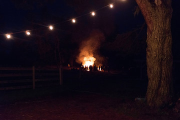 Silhouetted crowd watching bonfire in rural field at night