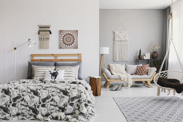 Hanging chair above carpet in spacious boho apartment interior with poster above bed. Real photo