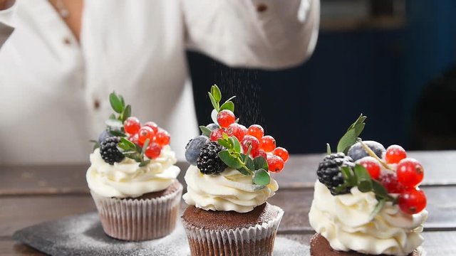 Baker decorating tasty cupcake. Icing sugar sprinkled on cake