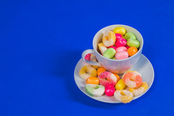 white Cup with sweet candy isolated on blue background.Close up selection of assorted colorful candy in bakery shop, .candy store. Party snack food concept. Copy space