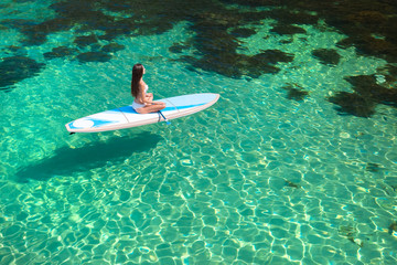 Young attractive woman meditating on the sup board in the sea. Girl in meditative pose on water.
