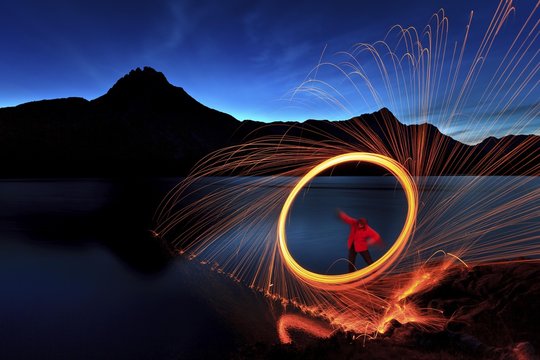Man with hoop of fire with sparks on the shore of the Spullersee, behind as silhouette the Plattnitzer Jochspitze, blue hour, long time exposure, Lake Spullersee, Lechquellen Mountains, Vorarlberg, Austria, Europe