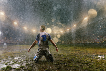 Soccer player on professional soccer night rain stadium. Dirty player in rain drops emotionally rejoices victory. Back view © Alex