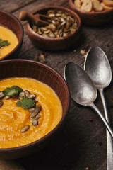 close-up view of delicious pumpkin soup in bowls and spoons on wooden table