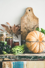Autumn seasonal food ingredients, kitchen utensils. Vegetables, pumpkin, canned food, fallen leaves over rustic wooden chest of cupboard, vertical composition Thanksgiving dinner preparation