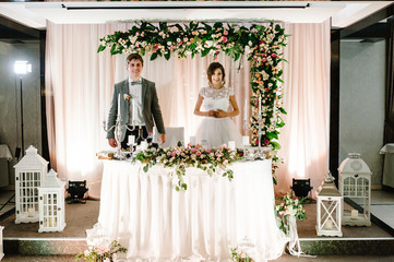 The happy bride and funny groom sit at the table and celebrate the wedding in the banquet hall of the restaurant. Newlyweds of the indoors.