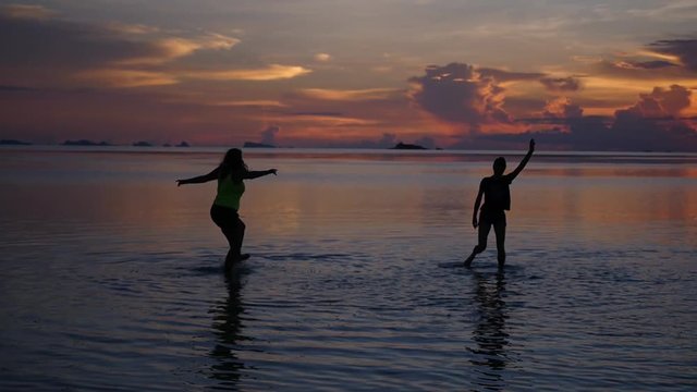 Two young girls enjoy life and dance in the water, admiring the beautiful sunset and its reflection in the sea. HD, 1920x1080, slow motion