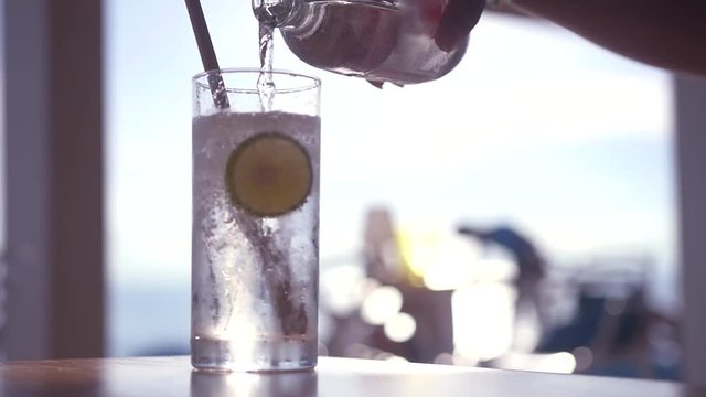 Pour refreshing sparkling water from a bottle into a glass with ice and a slice of lime. HD, 1920x1080, slow motion