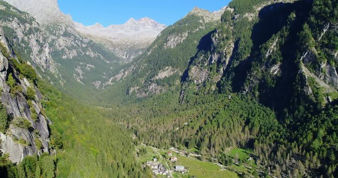 Flying over a little village in an alpine valley with forests and rock faces. Val di Mello, Valtellina, Italian Alps. This valley is famous for sport climbing. Aerial shot made with drone.